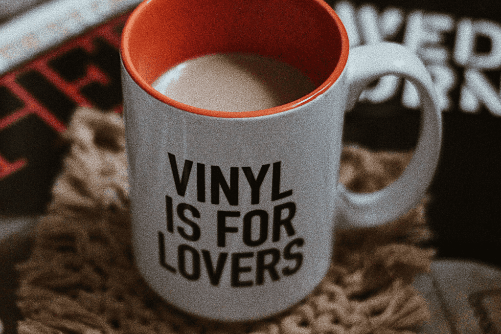Mug that says ‘vinyl is for lovers’ on a desk beside vinyl records – representing vinyl records wholesale culture